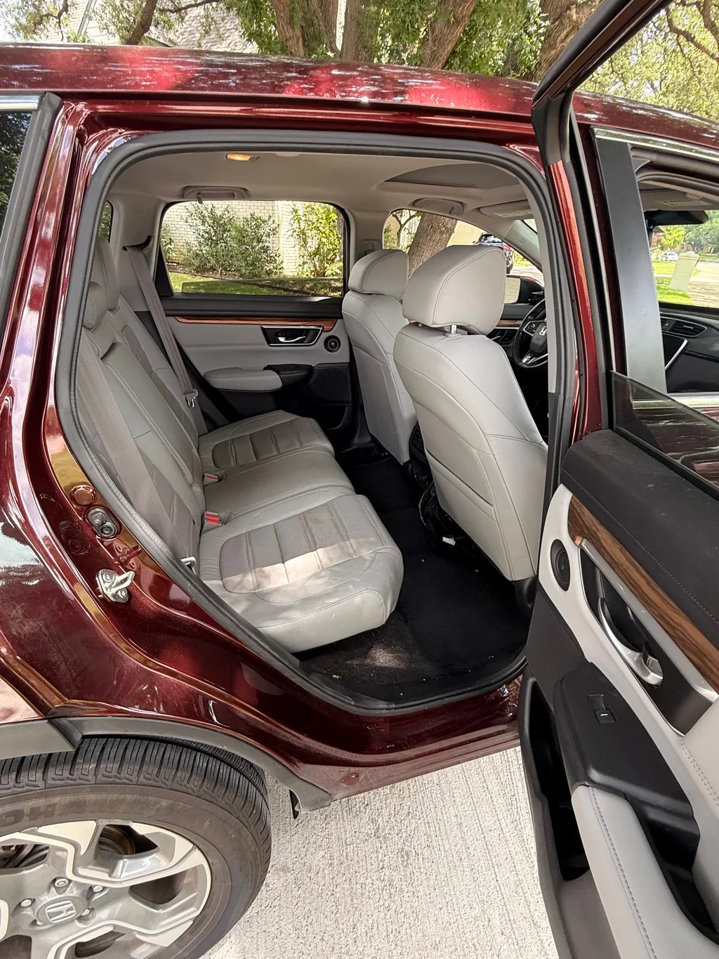 Rear seat of a red Honda CR-V before detailing, seen through the open door, with dirt and debris on the floor carpet