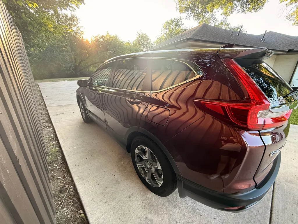 Rear three quarter view of a red Honda CR-V with glossy paint at sunset after an exterior detail, parked in a driveway beside a fence
