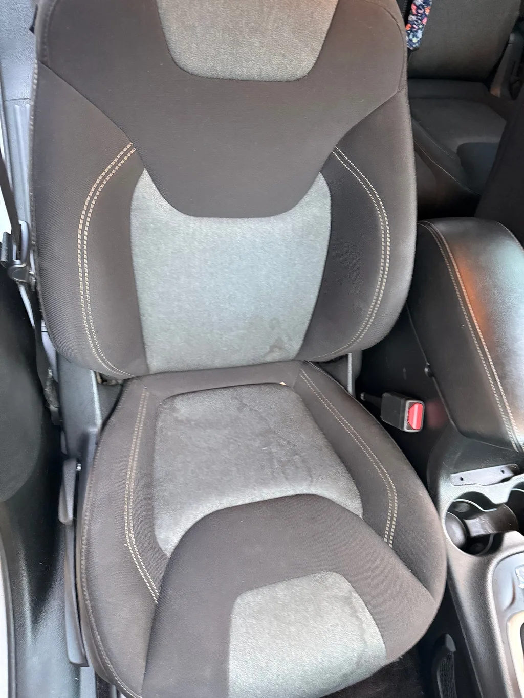 Driver seat of a silver Jeep Cherokee before detailing, with marks and dust on the grey cloth seat cushion