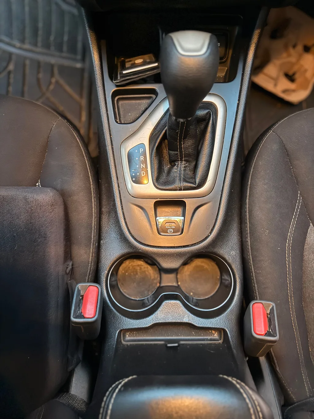Center console of a silver Jeep Cherokee before detailing, with dust in the cup holders and around the gear shifter
