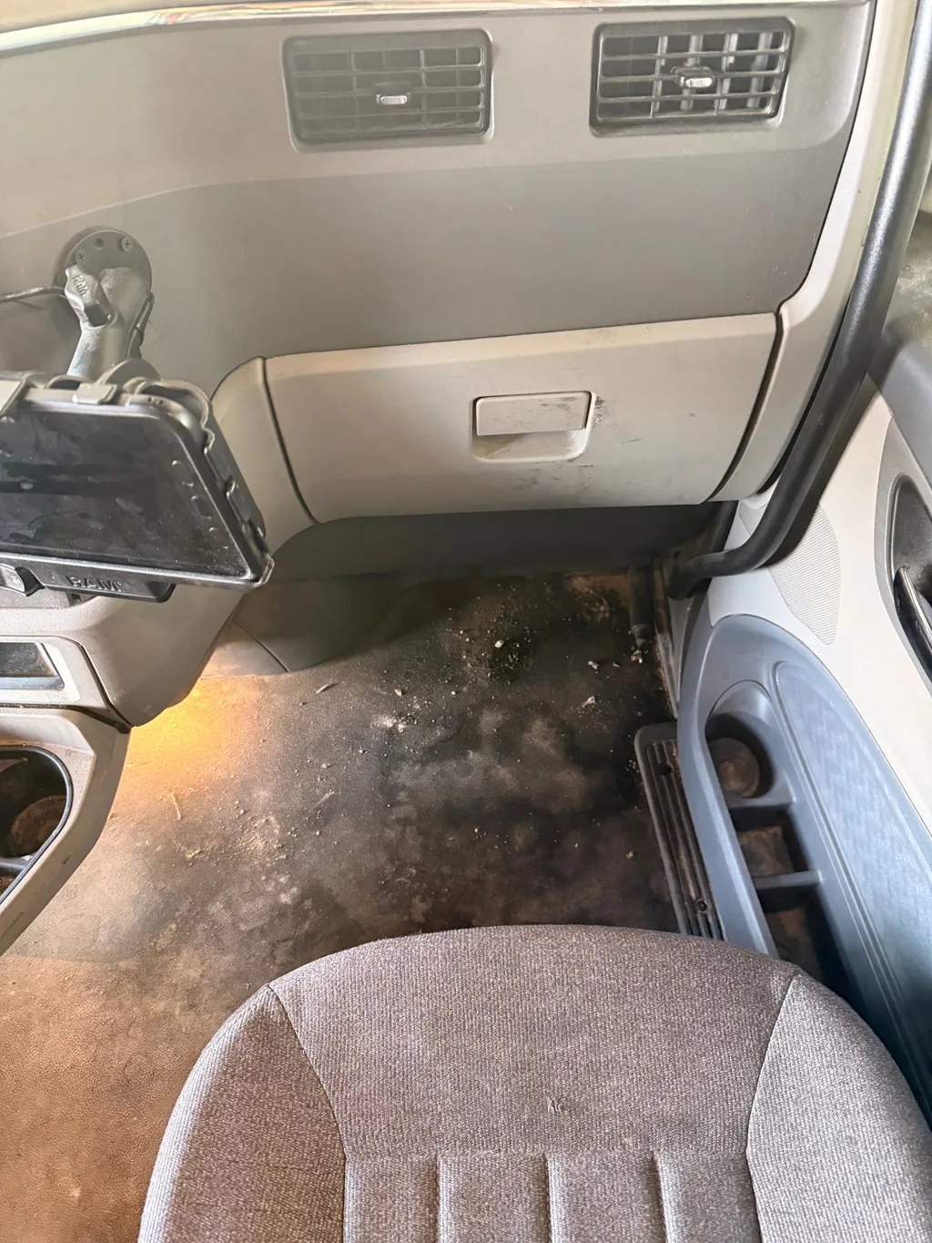 Passenger side of a semi truck cab before detailing, with dirt and debris on the floor under the glove box