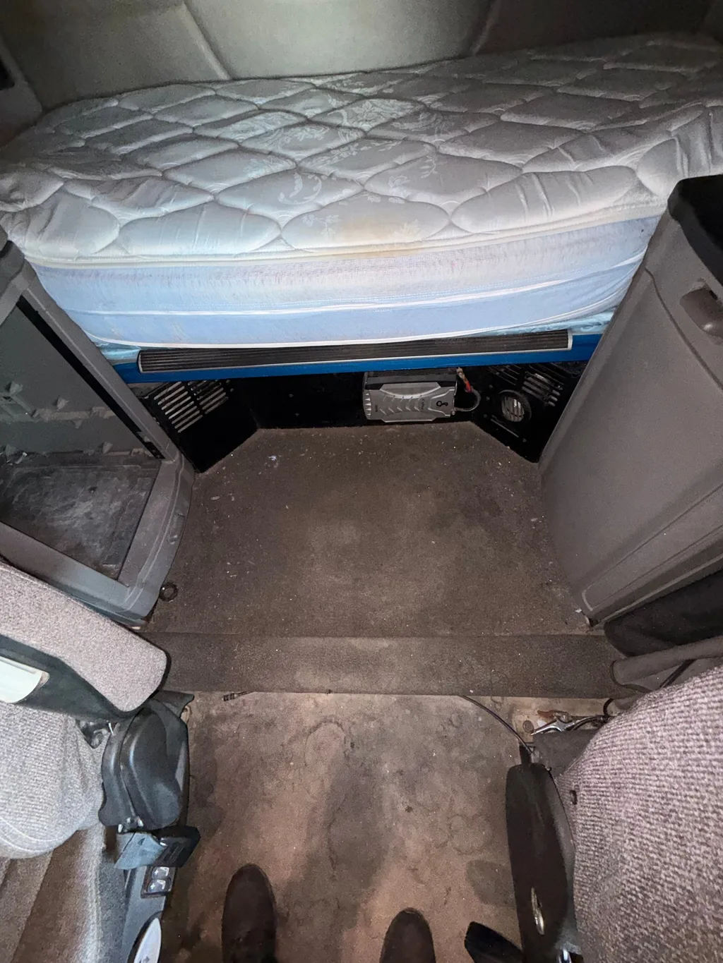 Semi truck sleeper before detailing, bare mattress above a dirty floor marked with boot prints