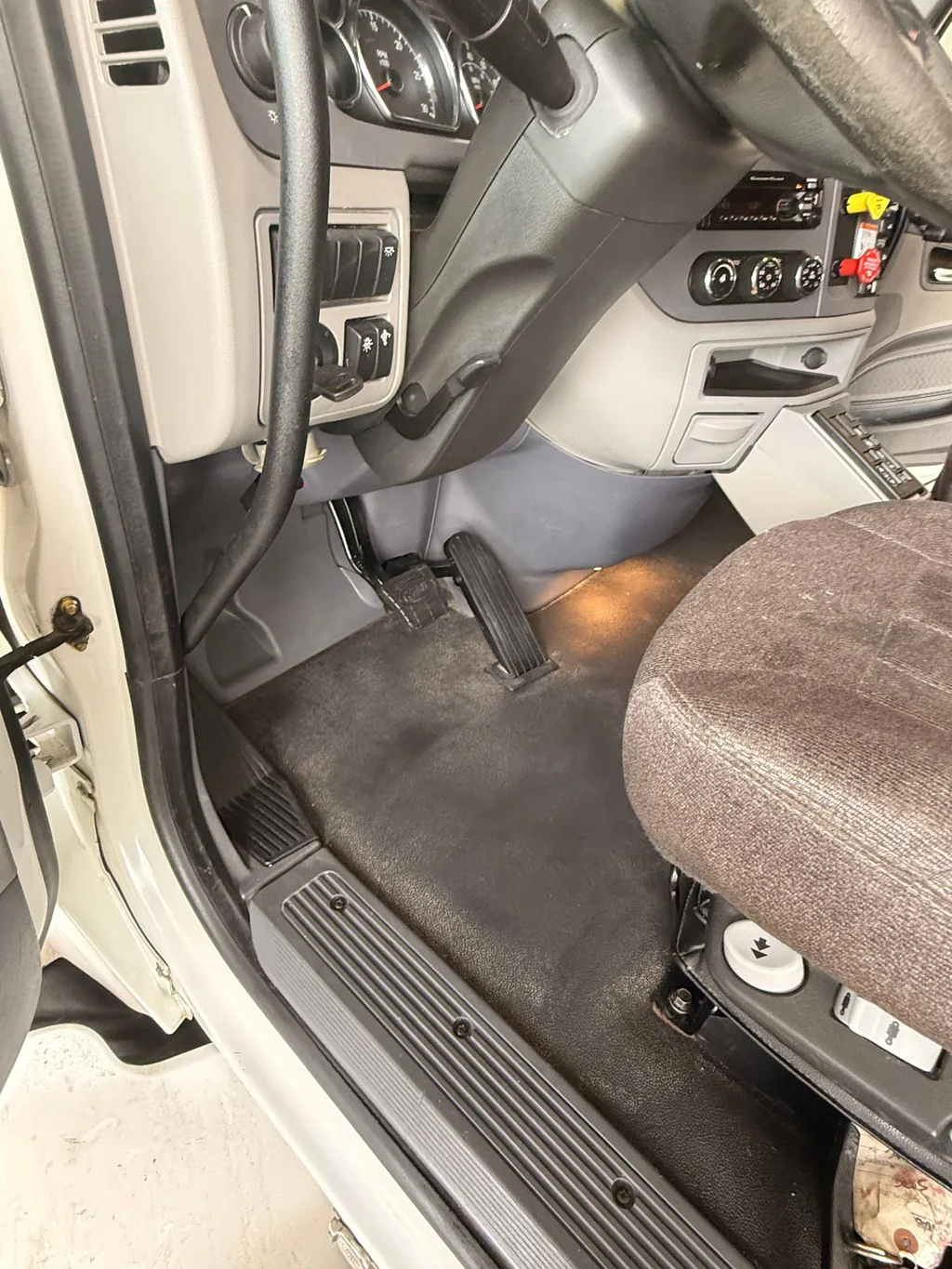 Driver side floor of the semi truck cab after an interior detail, dark floor covering and door sill clean